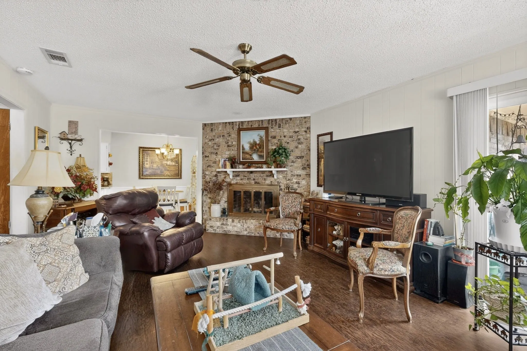 Wood-finish flooring, ceiling fan, brick fireplace, and vertical paneling