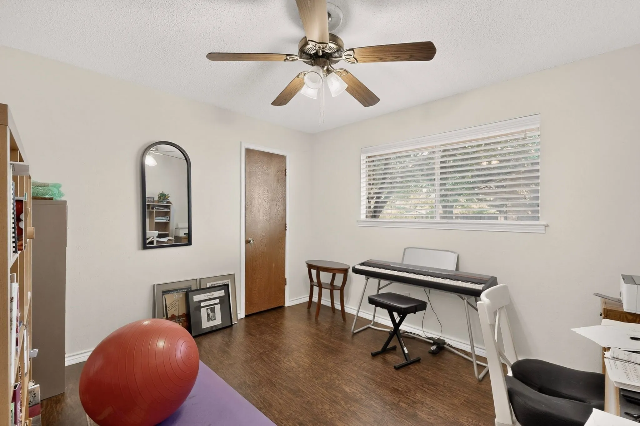 Wood-finish flooring, ceiling fan with integrated lighting, and a large window with blinds