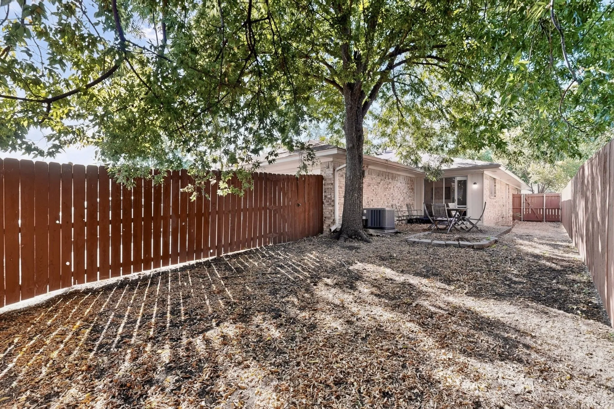 Private backyard featuring a wood privacy fence, mature trees, and a stone patio