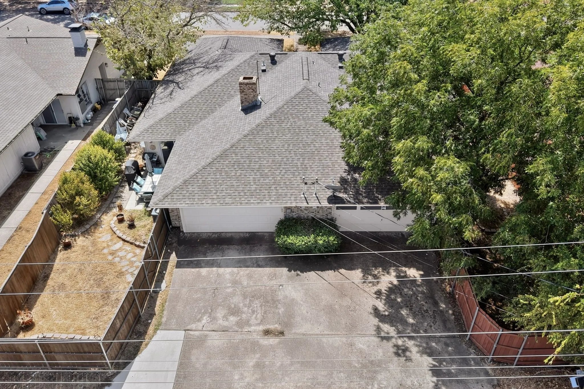Asphalt shingle roof, brick chimney, attached garage, mature trees, and fenced perimeter