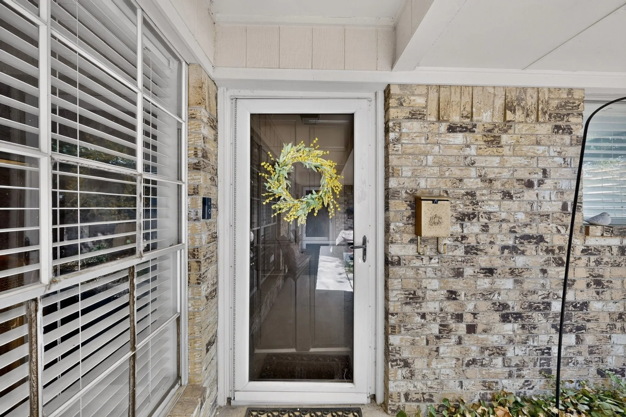 Brick exterior with a white storm door, side window with blinds, and a wall-mounted mailbox