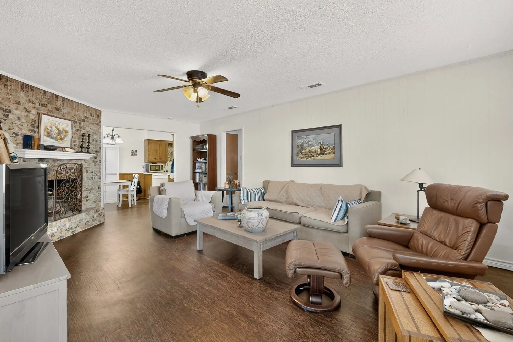 Brick-clad fireplace with a white mantel, wood-finish flooring, and a ceiling fan with integrated lighting