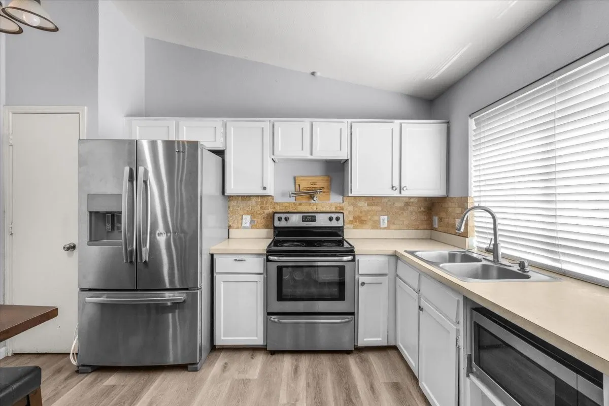 Kitchen featuring stainless steel appliances, light-toned countertops, white cabinetry, a tile backsplash, and wood-finish flooring