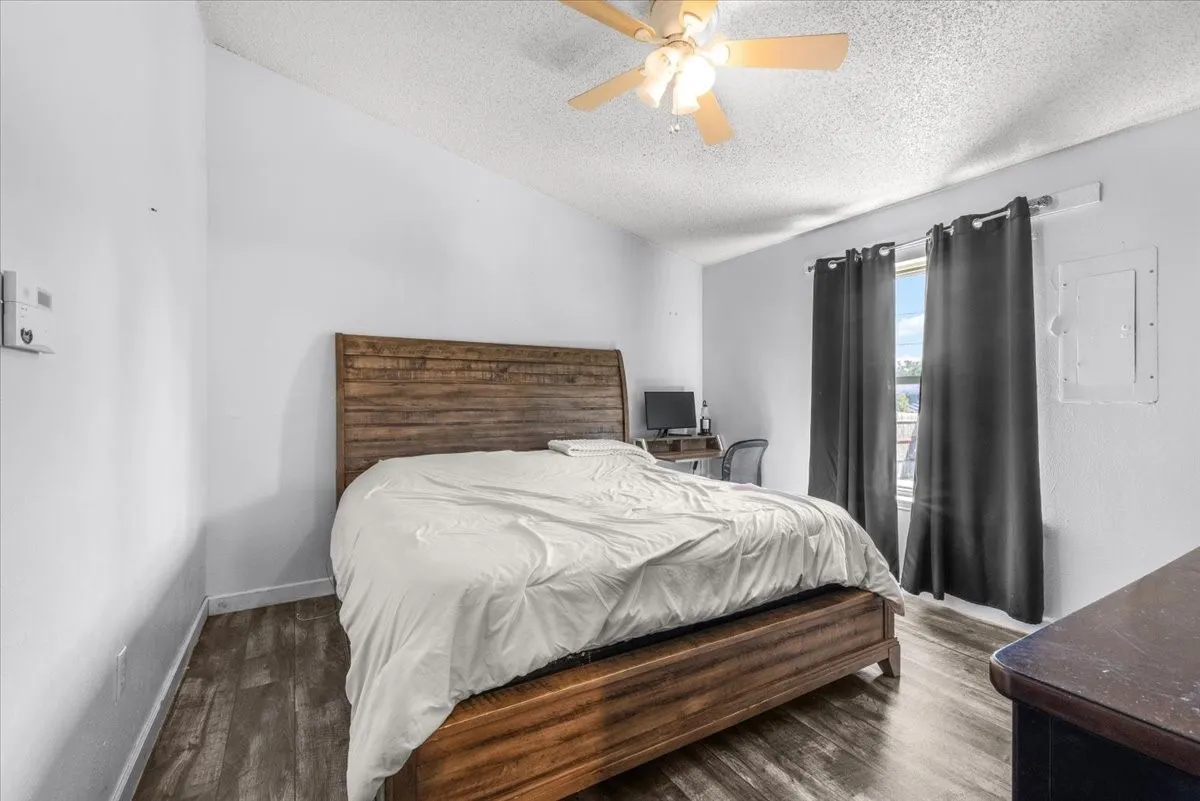 Wood-finish flooring throughout, ceiling fan with integrated lighting, and window with dark drapery