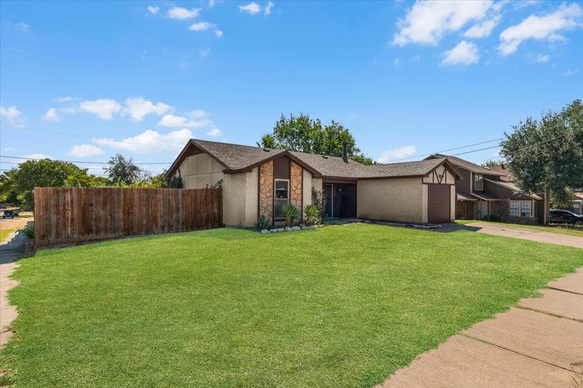 Expansive front lawn, wood fence, attached garage, stone facade accent, and mature landscaping