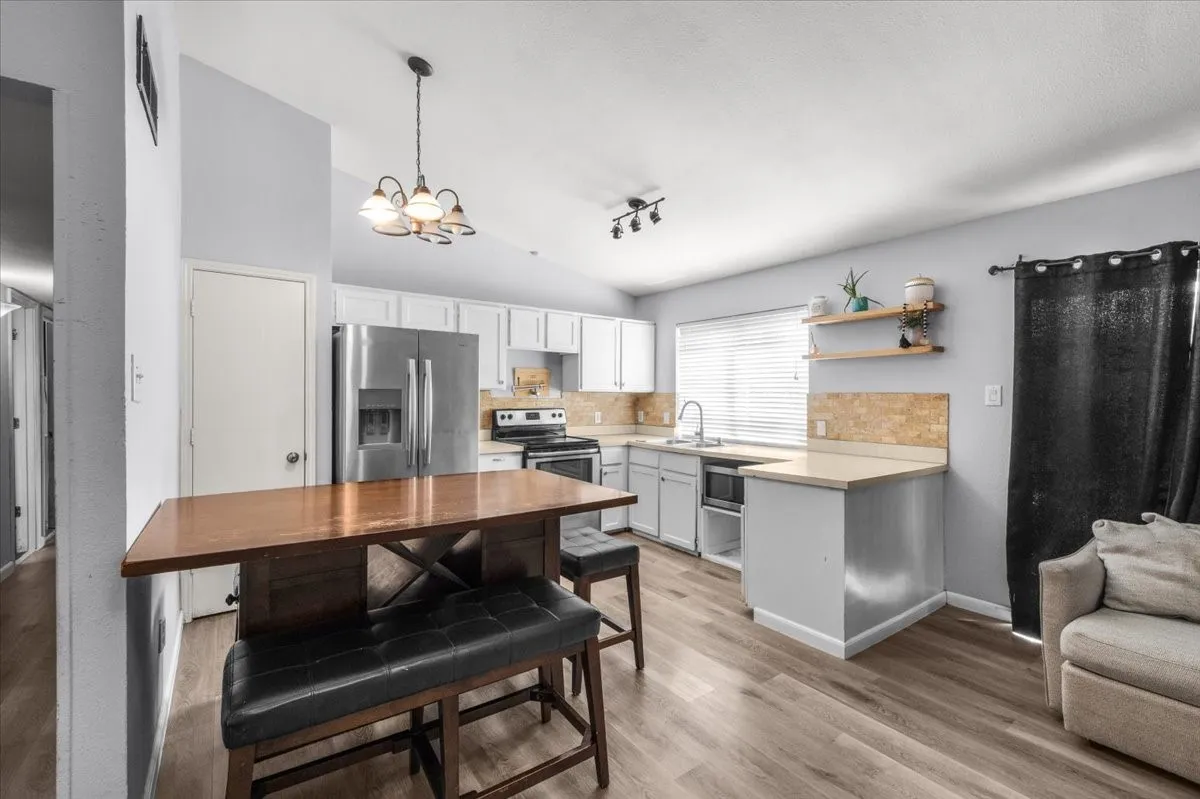 Modern kitchen featuring stainless steel appliances, white cabinetry, light countertops, wood-finish flooring, and a breakfast bar