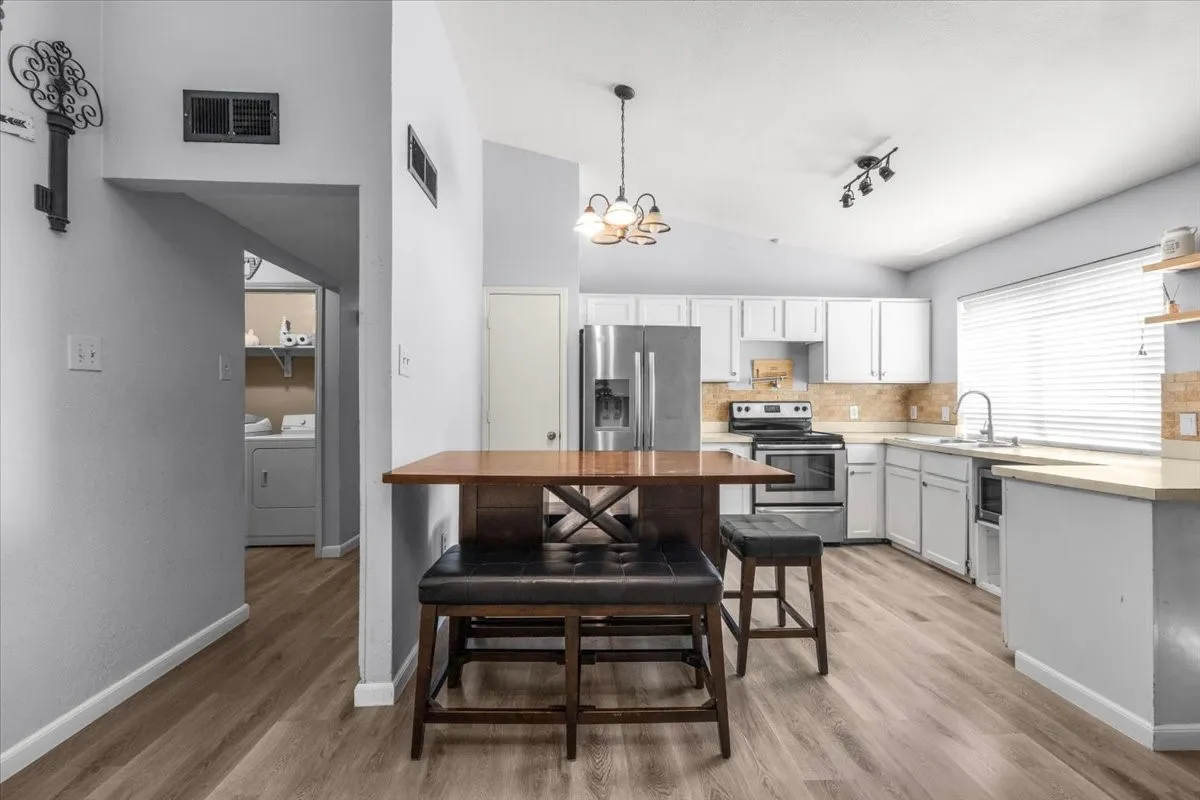 Vaulted ceiling kitchen featuring wood-finish flooring, white cabinetry, stainless steel appliances, and a tiled backsplash