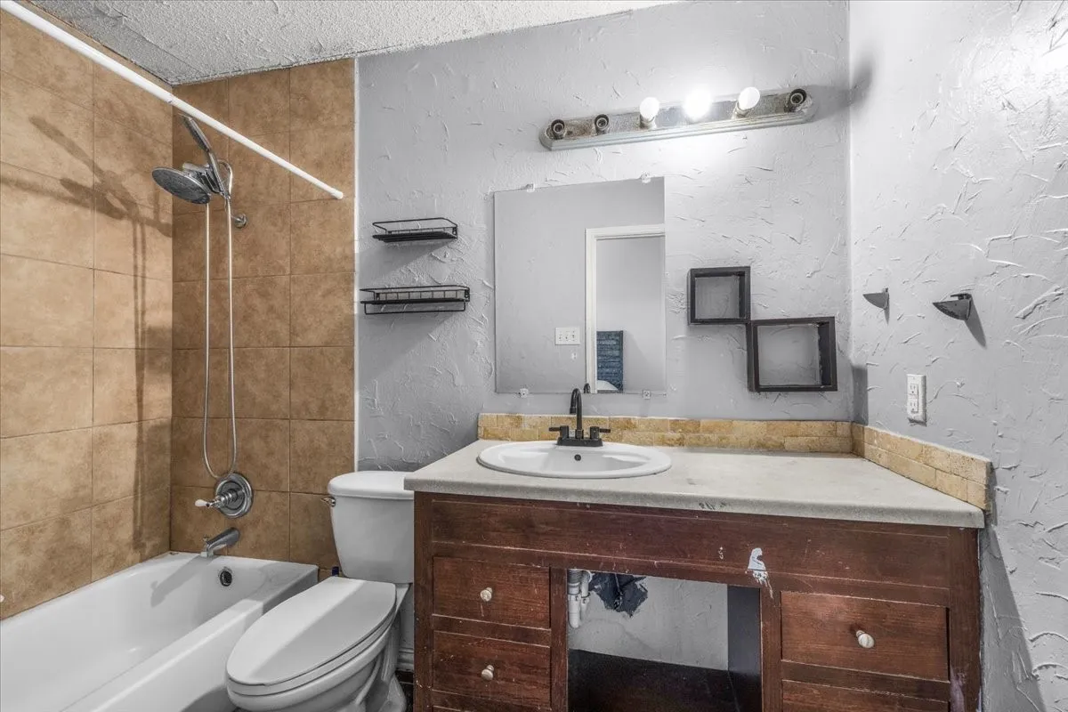 Bathtub with tiled surround, wood-finish vanity with countertop, and wall-mounted mirror