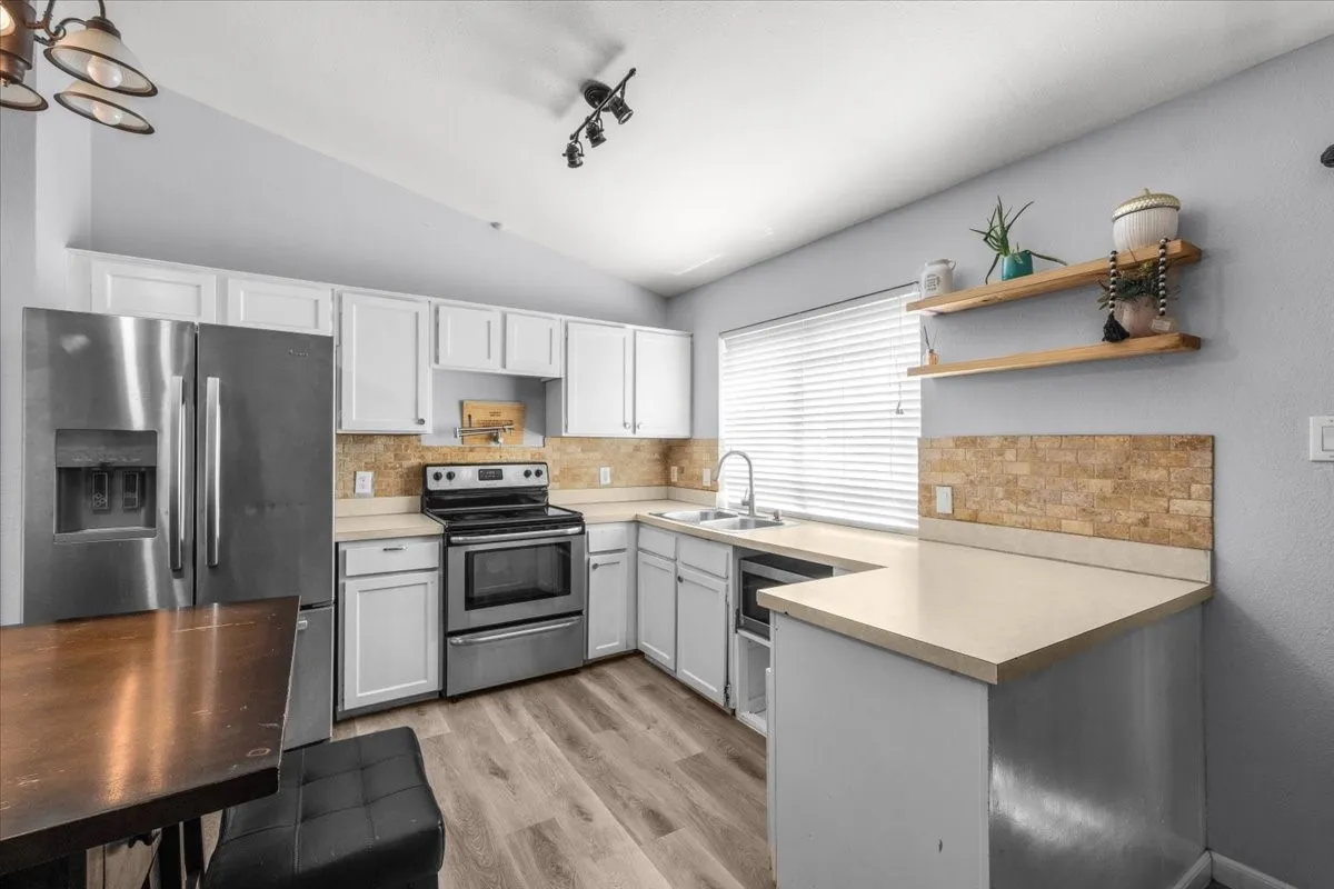 Kitchen featuring wood-finish flooring, white cabinetry, stainless steel appliances, and a tiled backsplash