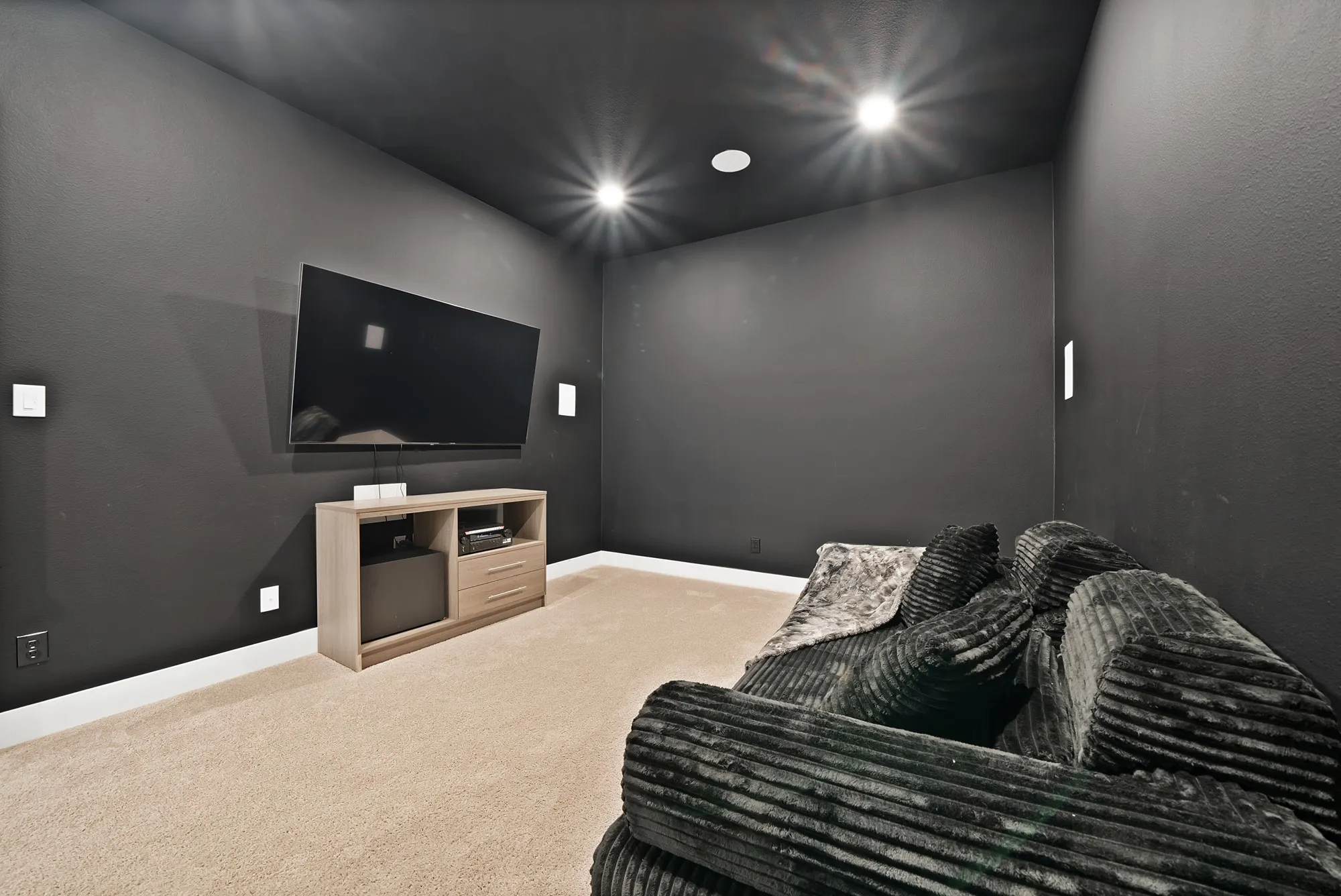 Recessed ceiling lighting, wall-mounted display, light-toned carpeting, and a built-in media console
