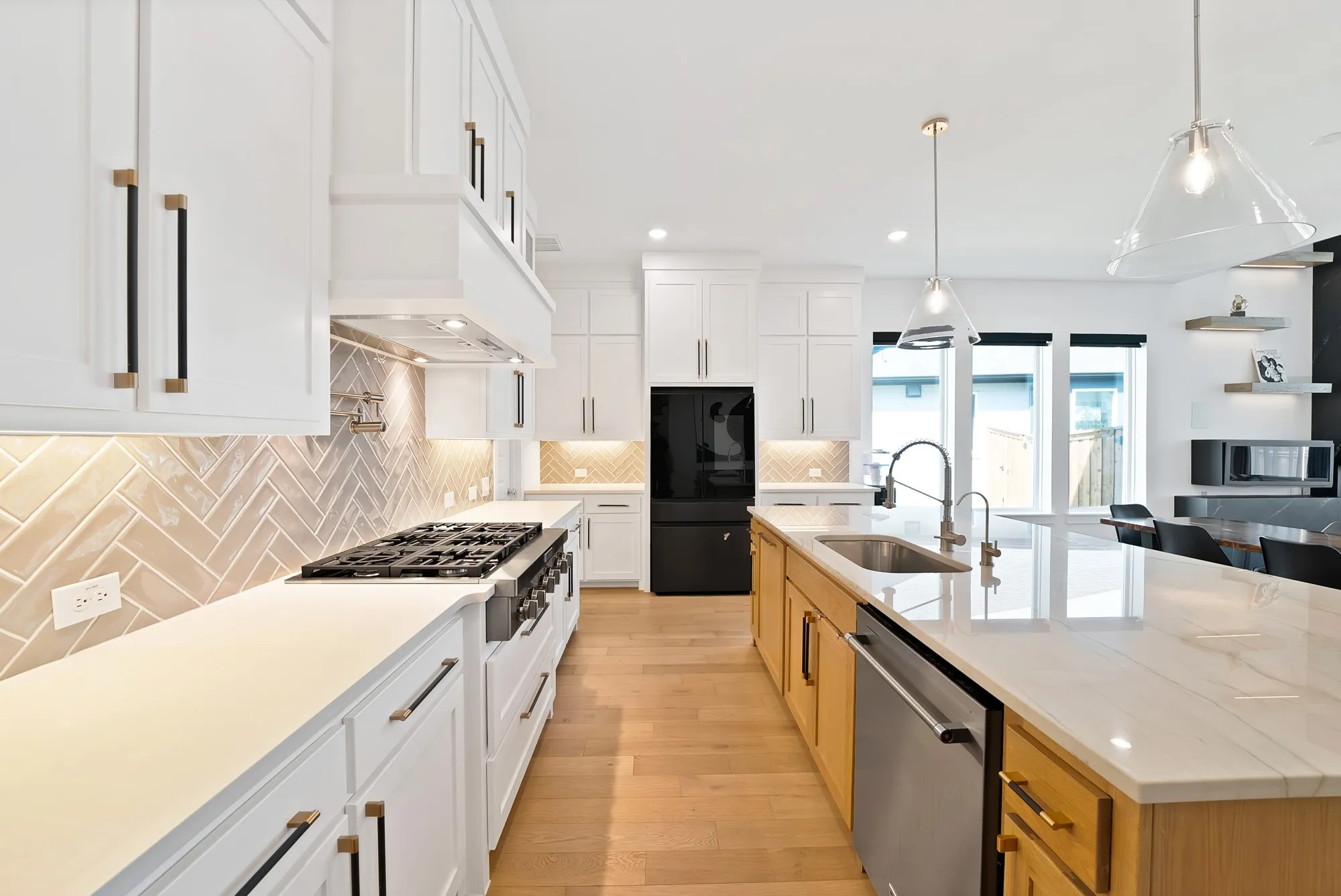 White shaker cabinetry, herringbone tile backsplash, stainless steel appliances, central island with sink, and wood-finish flooring