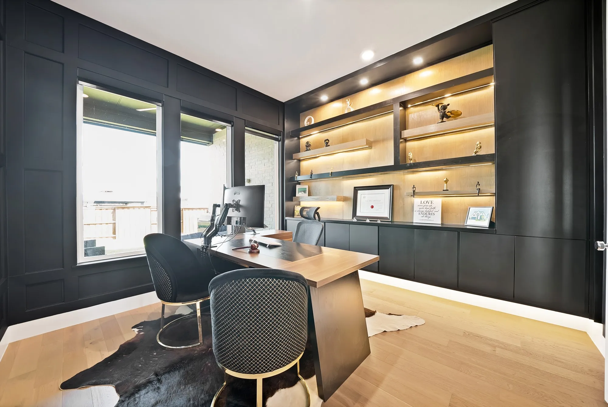 Light wood-finish flooring, built-in shelving with integrated lighting, built-in lower cabinetry, and dark paneled walls
