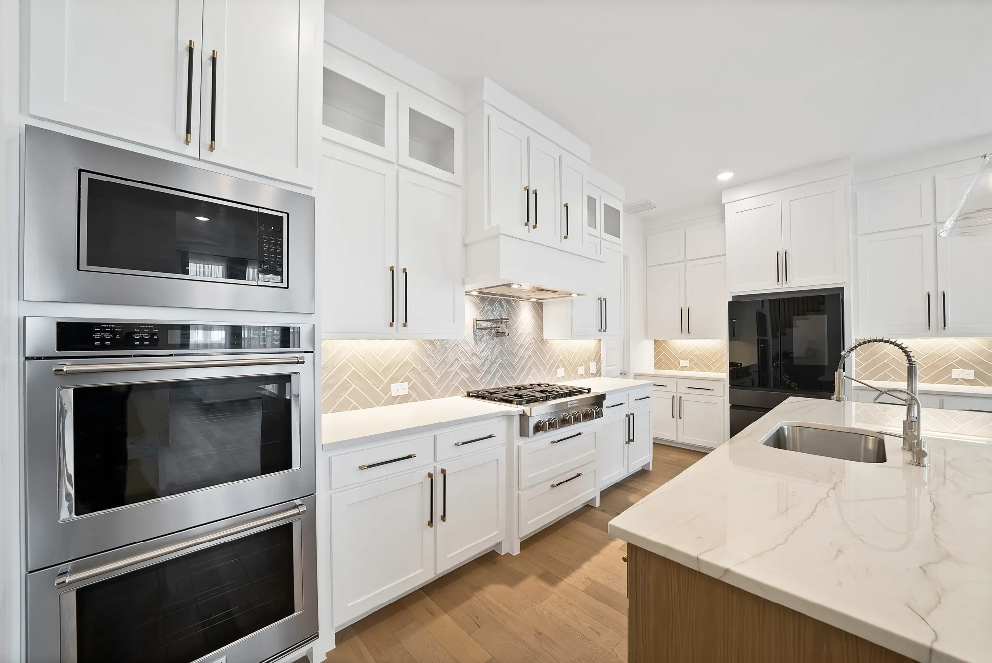 Gourmet kitchen featuring white shaker cabinetry, stainless steel appliances, herringbone tile backsplash, and a large central island with an undermount sink