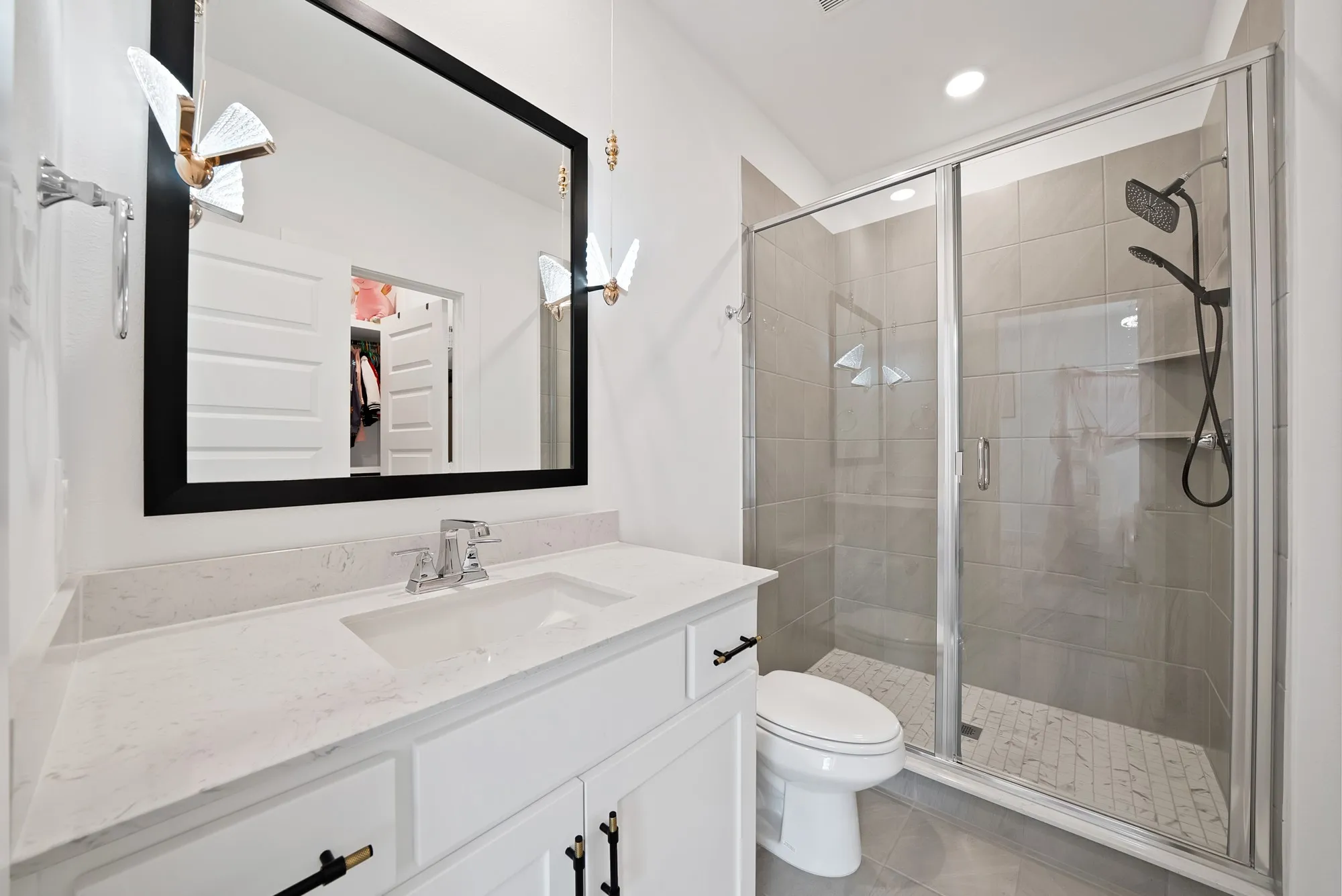 White vanity with a light-colored countertop, wall-mounted mirror, and glass-enclosed shower with a rainfall​​‌​​​​‌​​‌‌​‌‌​​​‌‌​‌​‌​‌​​​‌​​ showerhead