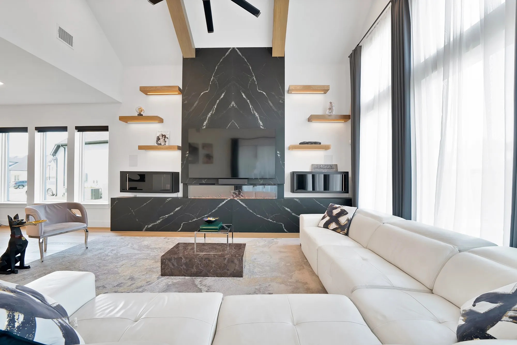 Vaulted ceilings, a full-height dark marble-finish accent wall with integrated fireplace, recessed lighting, and large windows with privacy coverings