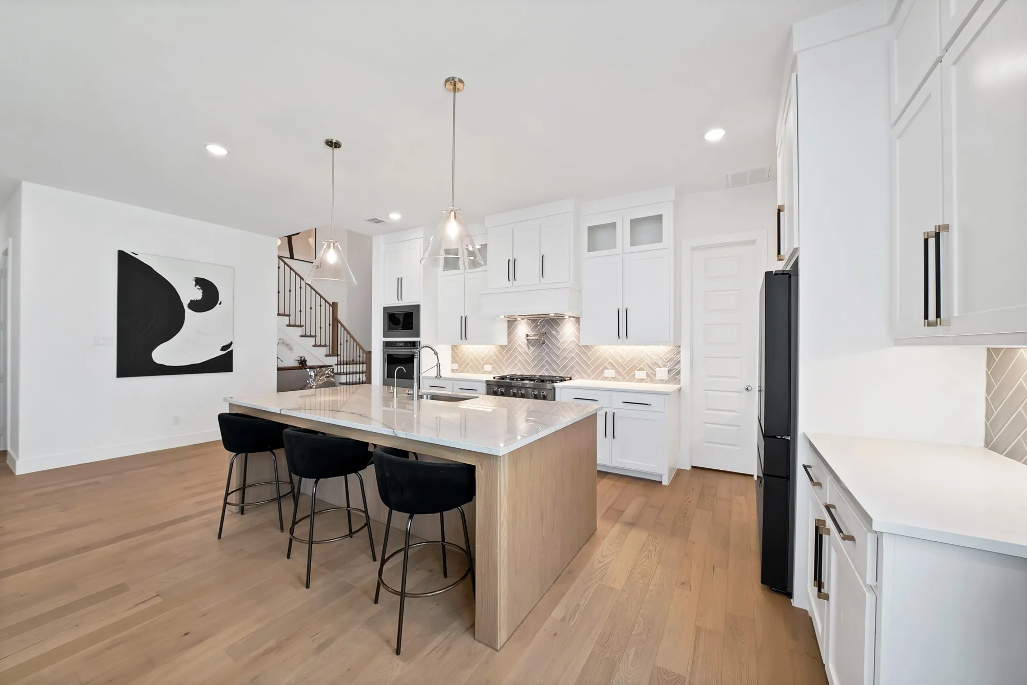 Gourmet kitchen featuring a large central island, light wood-finish flooring, white cabinetry with contemporary hardware, and a herringbone-patterned tile backsplash