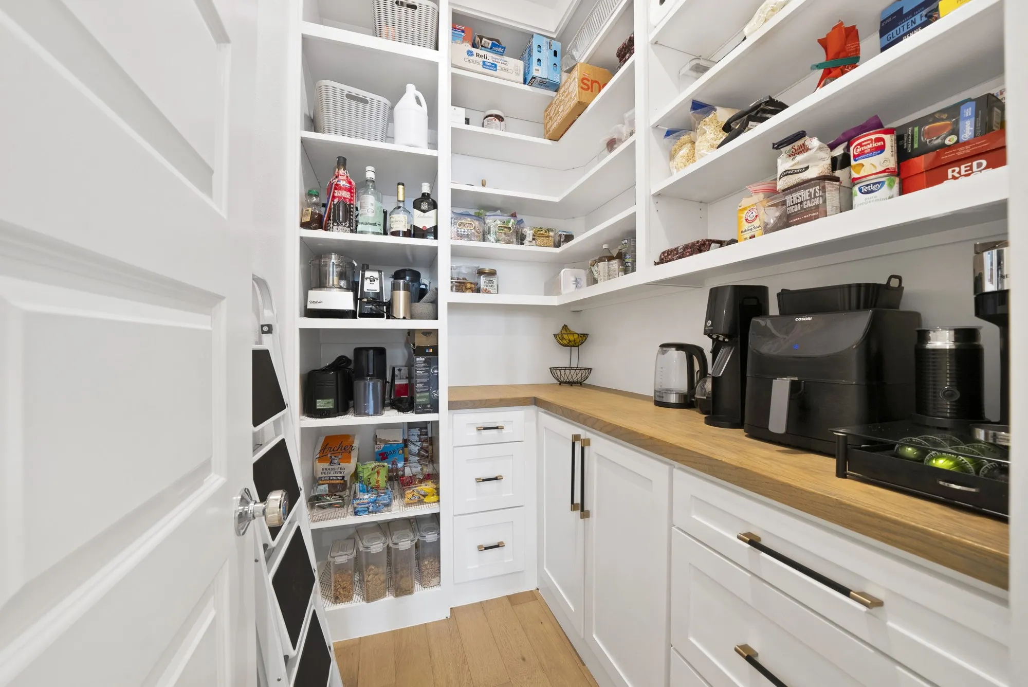 White shaker-style cabinetry with gold-tone hardware, wood-finish countertops, and extensive built-in shelving