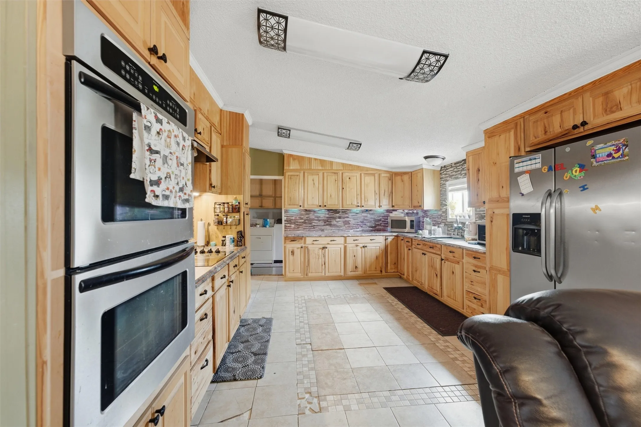 Kitchen featuring stainless steel double ovens, wood cabinetry, tile flooring, stone-finish backsplash, and recessed lighting