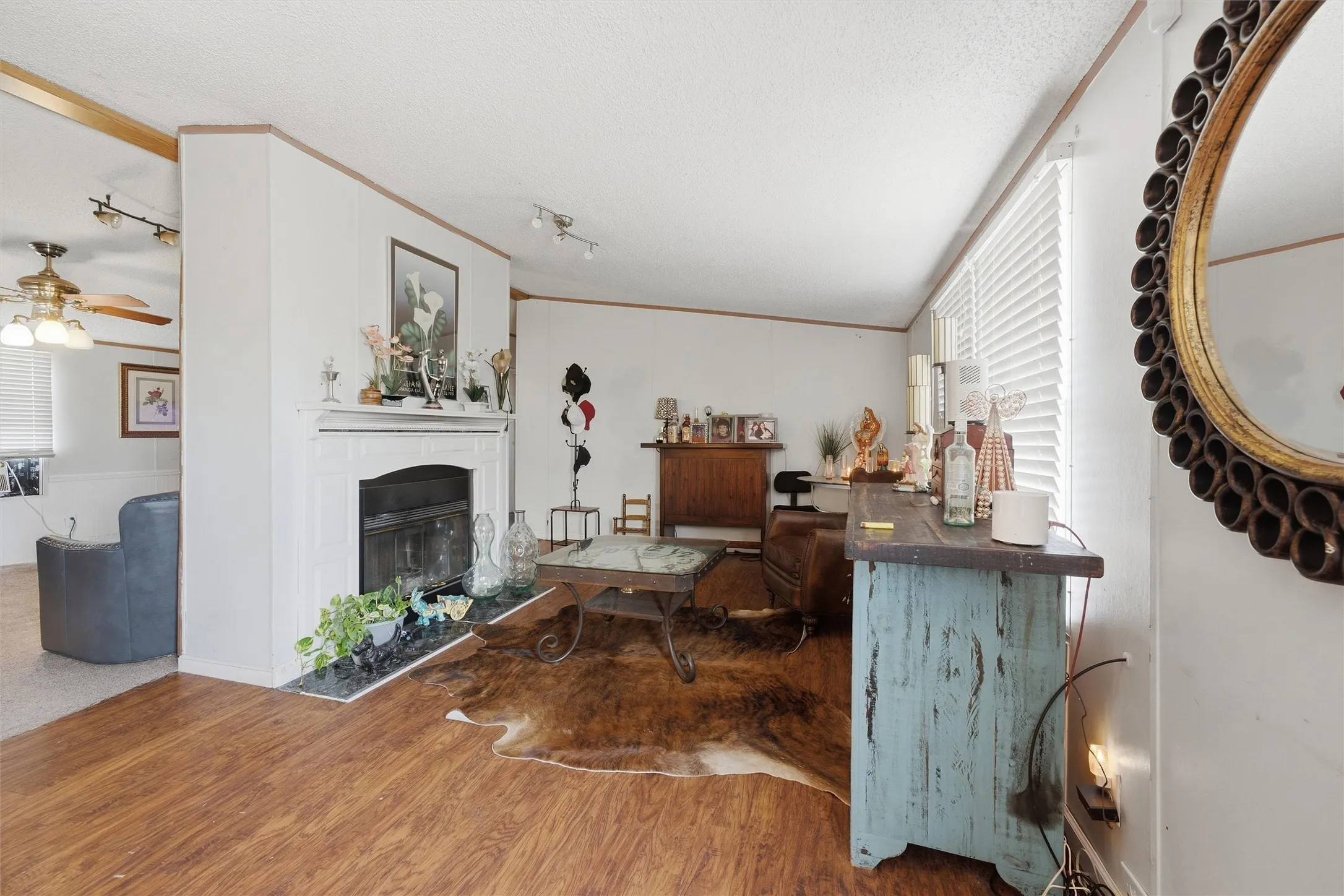 Fireplace with a stone hearth, wood-finish flooring, white horizontal blinds, and a ceiling fan with integrated lighting