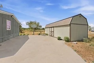 Exterior featuring a metal-sided building with a gambrel roof and an adjacent concrete pad