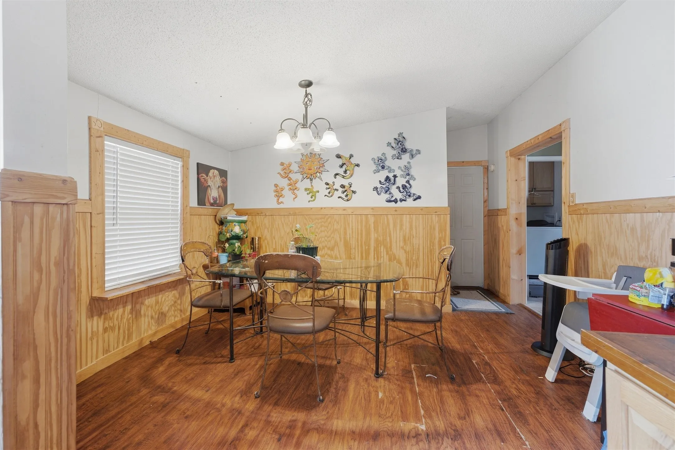 Wood-finish flooring, wood paneling, white walls, window with blinds, and an overhead chandelier