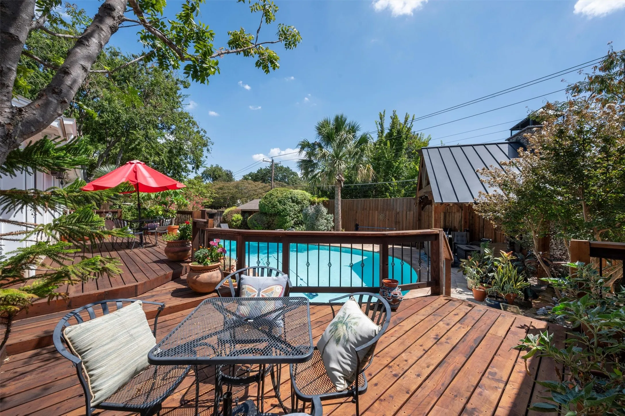 Expansive multi-level wood deck, outdoor pool, privacy fencing, mature landscaping, and a detached structure with a metal roof