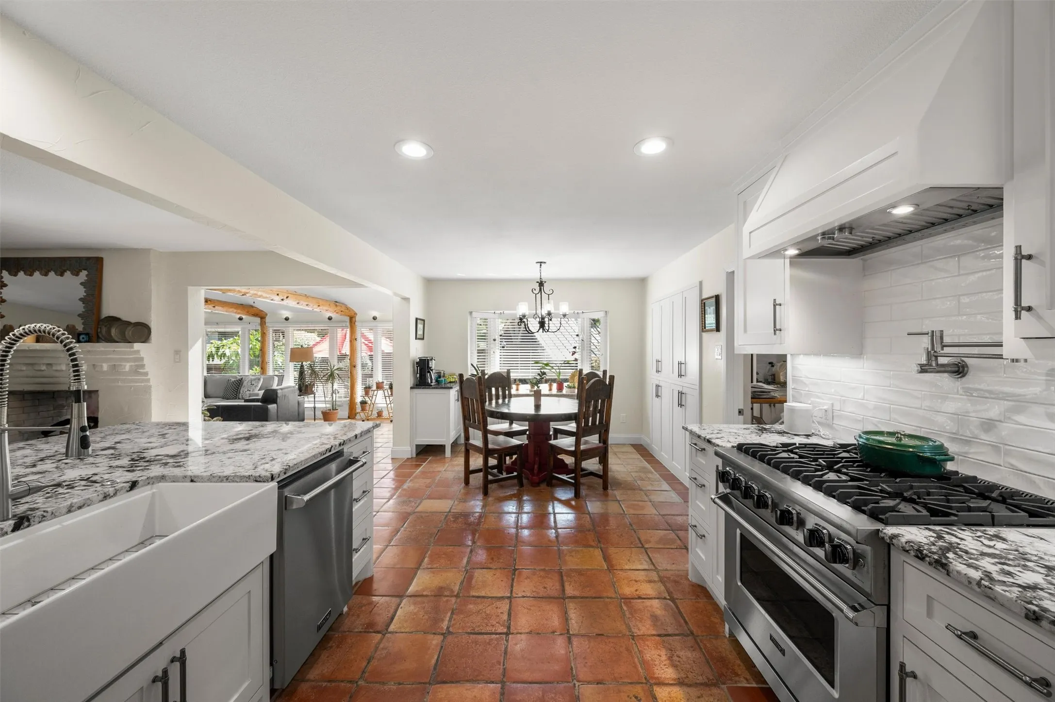 Gourmet kitchen featuring granite countertops, a farmhouse sink, stainless steel appliances, and a decorative range hood