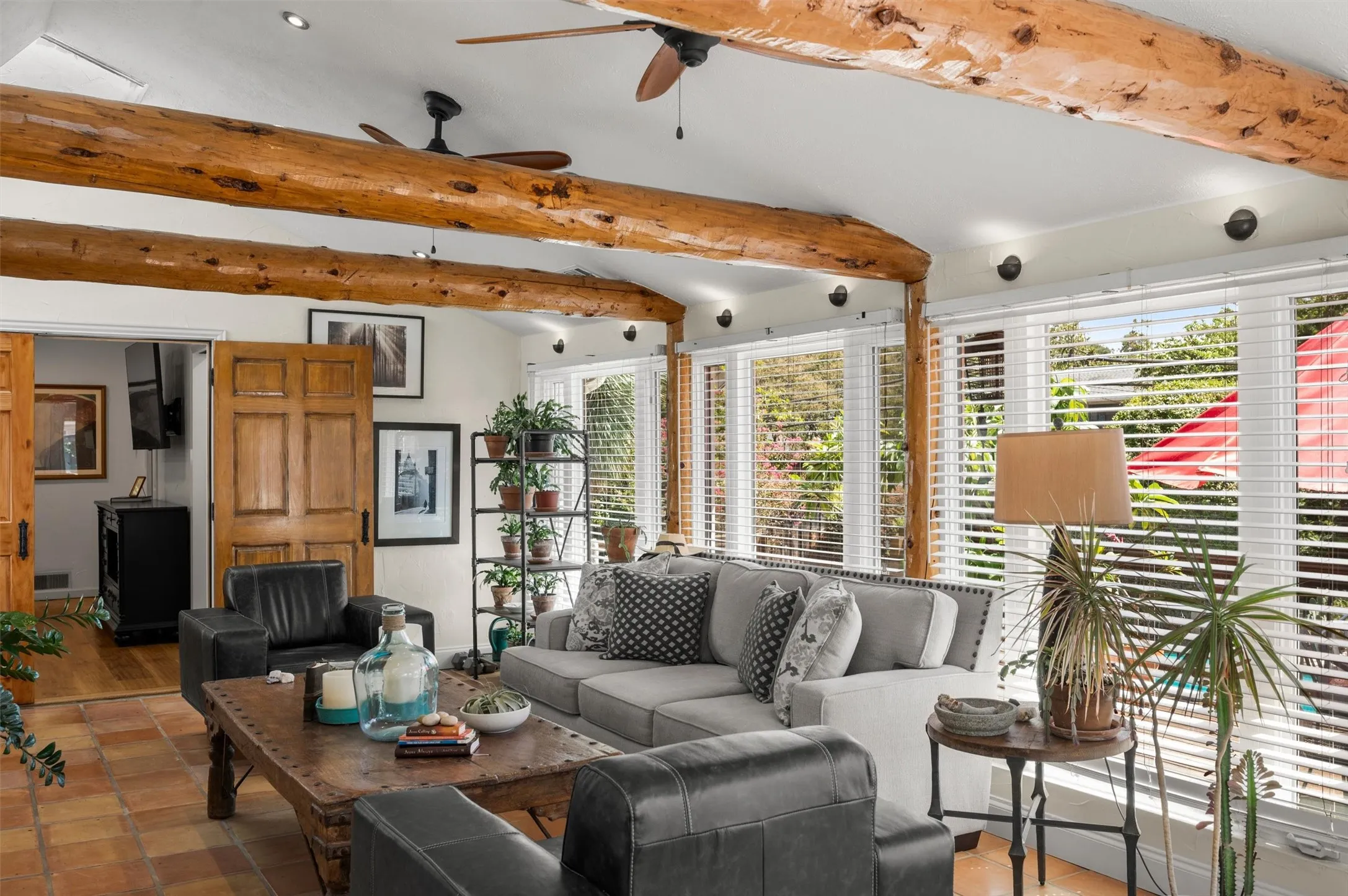 Vaulted ceiling with exposed wood beams, recessed lighting, terra cotta tile flooring, multiple windows with blinds, and wood double doors