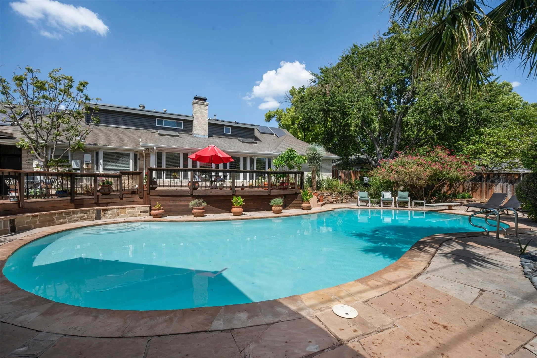 Expansive backyard featuring a curved swimming pool, surrounding stone patio, and a raised wood deck with railing