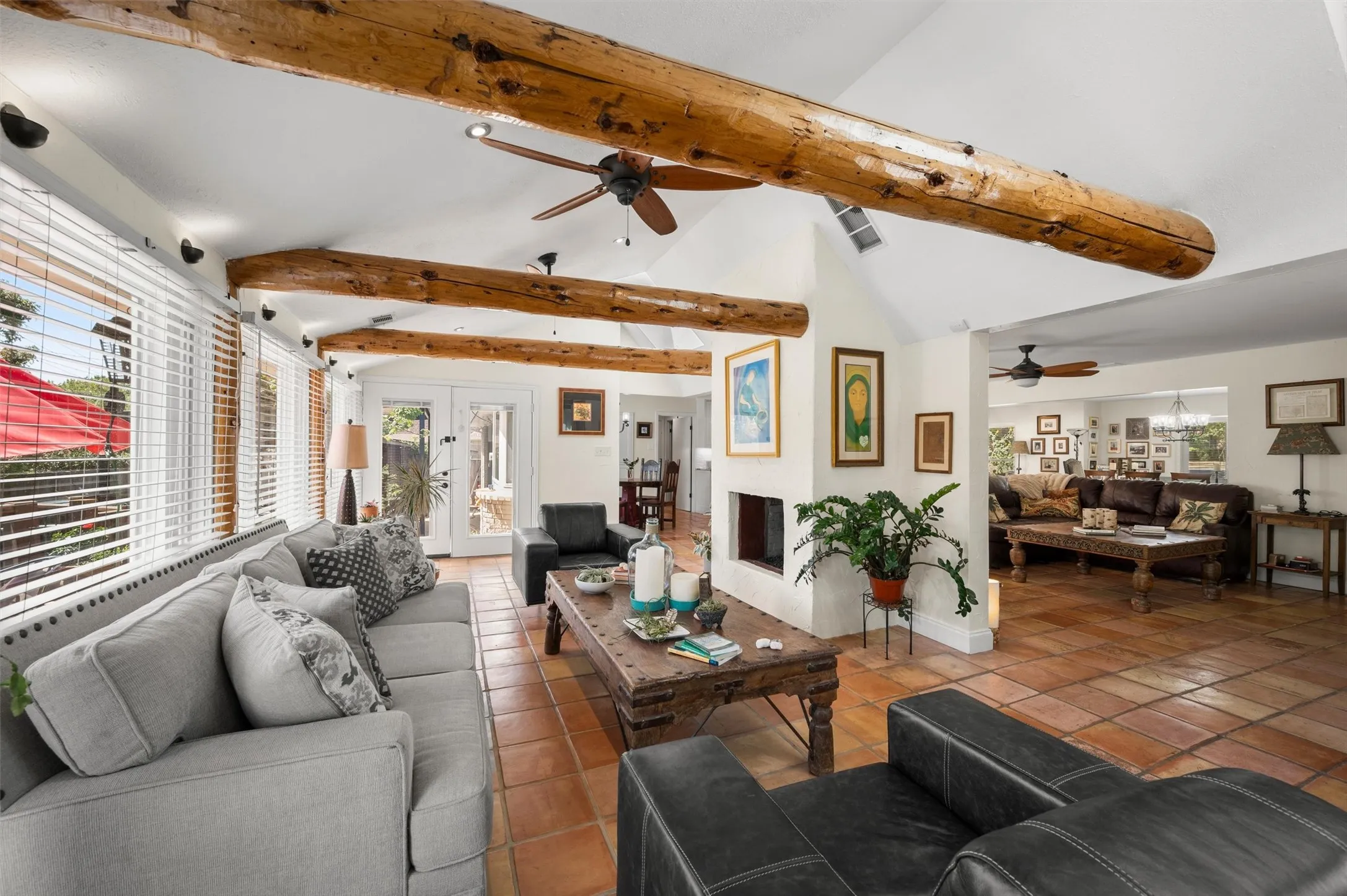 Vaulted ceiling with exposed wood beams, terracotta tile flooring, built-in fireplace, multiple ceiling fans, and French doors