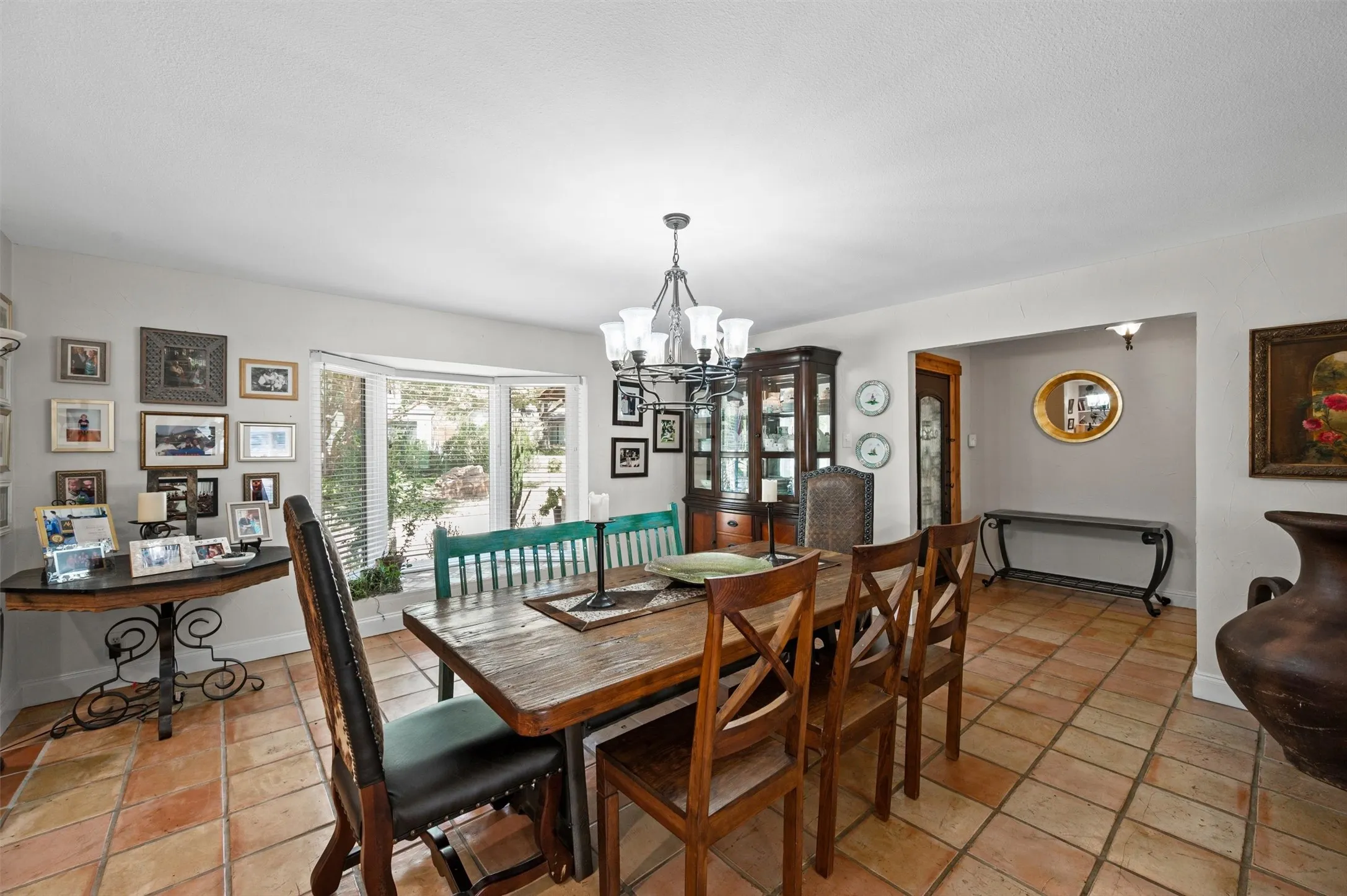 Terracotta tile flooring, bay window, chandelier lighting, built-in display cabinet, and arched entryway