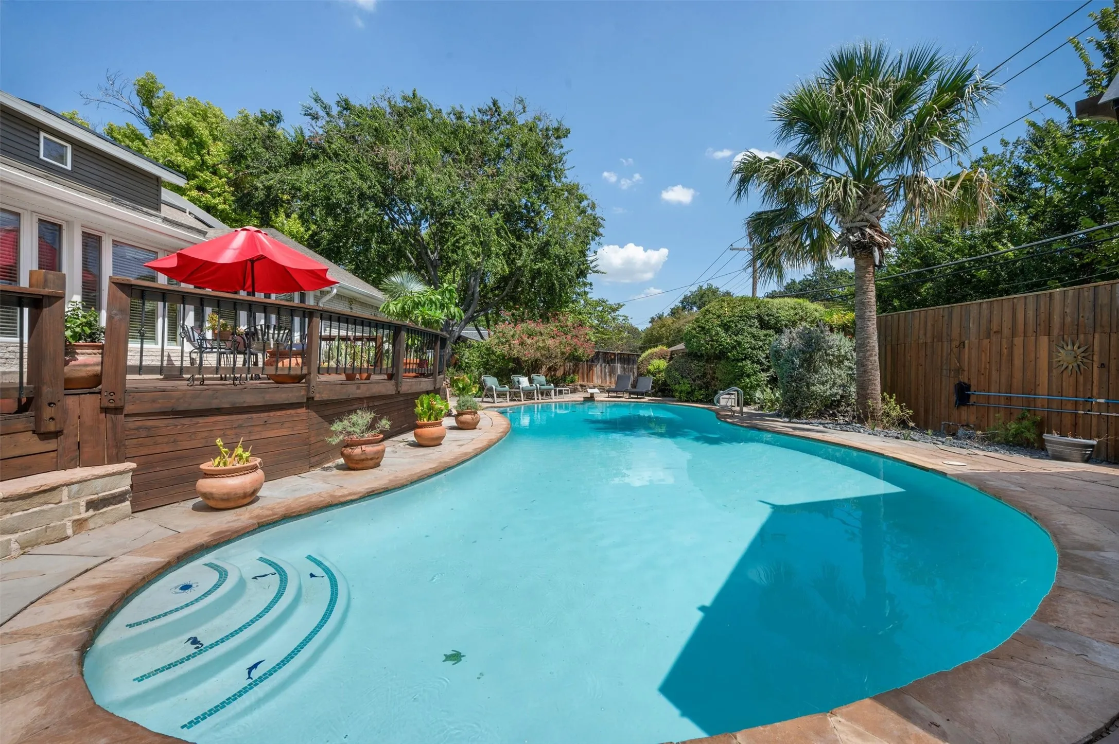 Curved swimming pool with integrated steps, surrounded by flagstone coping and a wooden privacy fence