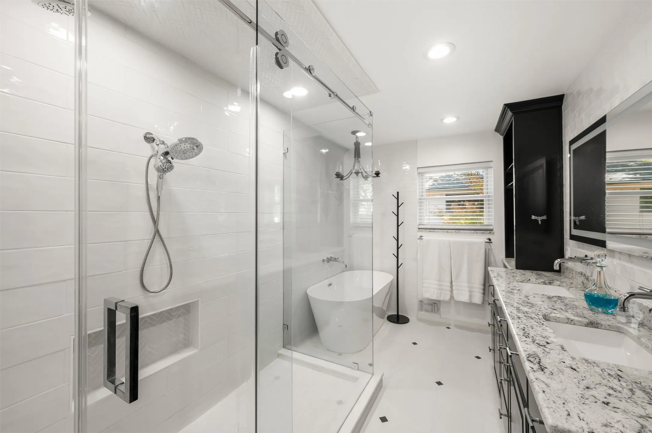 Glass-enclosed shower with subway tile, freestanding soaking tub, dual vanity with undermount sinks, stone countertop, and built-in storage cabinetry