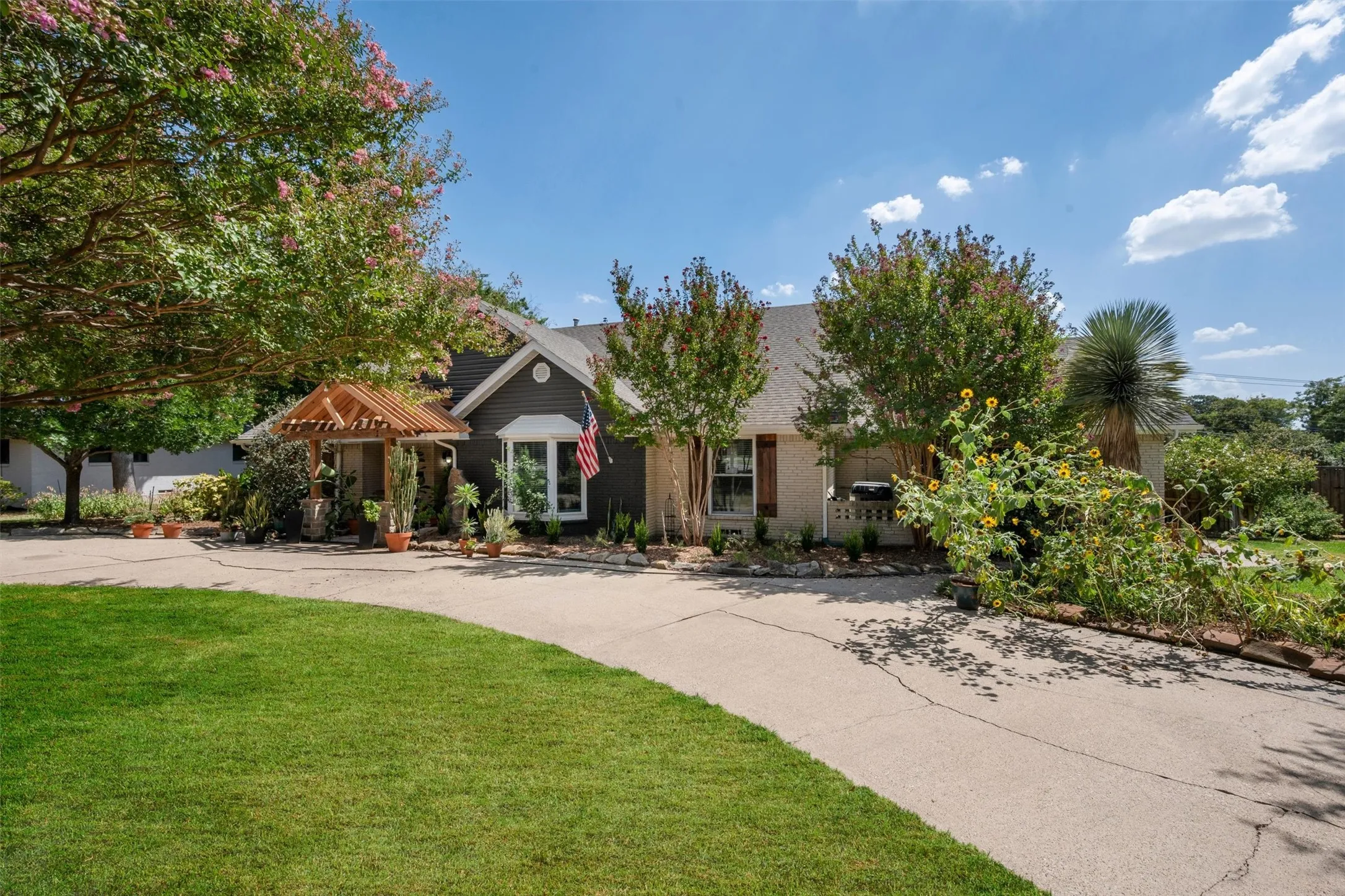 Manicured lawn with a curved paved driveway, featuring a front entry pergola and mature landscaping