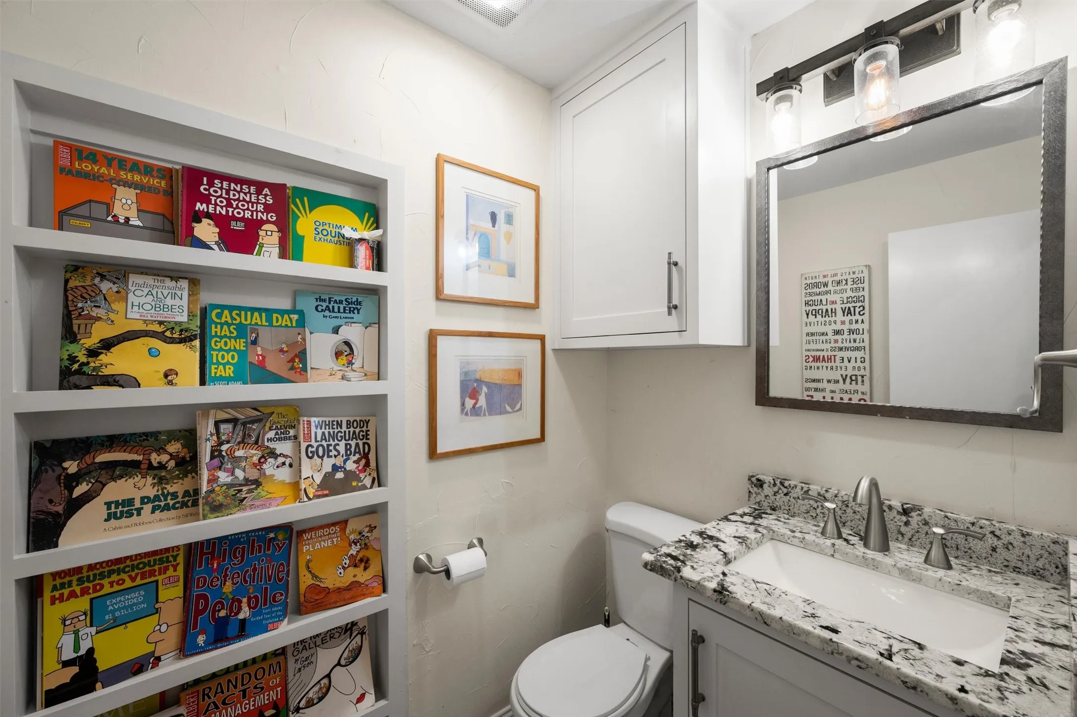 Built-in shelving unit, white vanity with stone-finish countertop, single basin sink, and wall-mounted lighting fixture