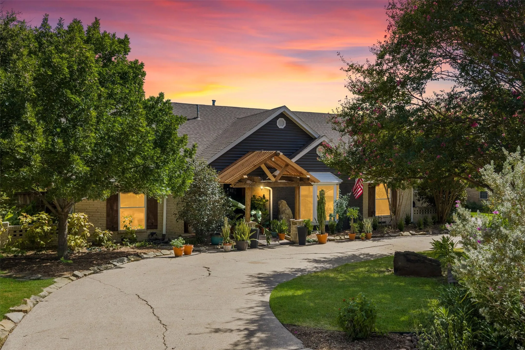 Exterior featuring a concrete driveway, mature trees, a covered entrance, and shuttered windows