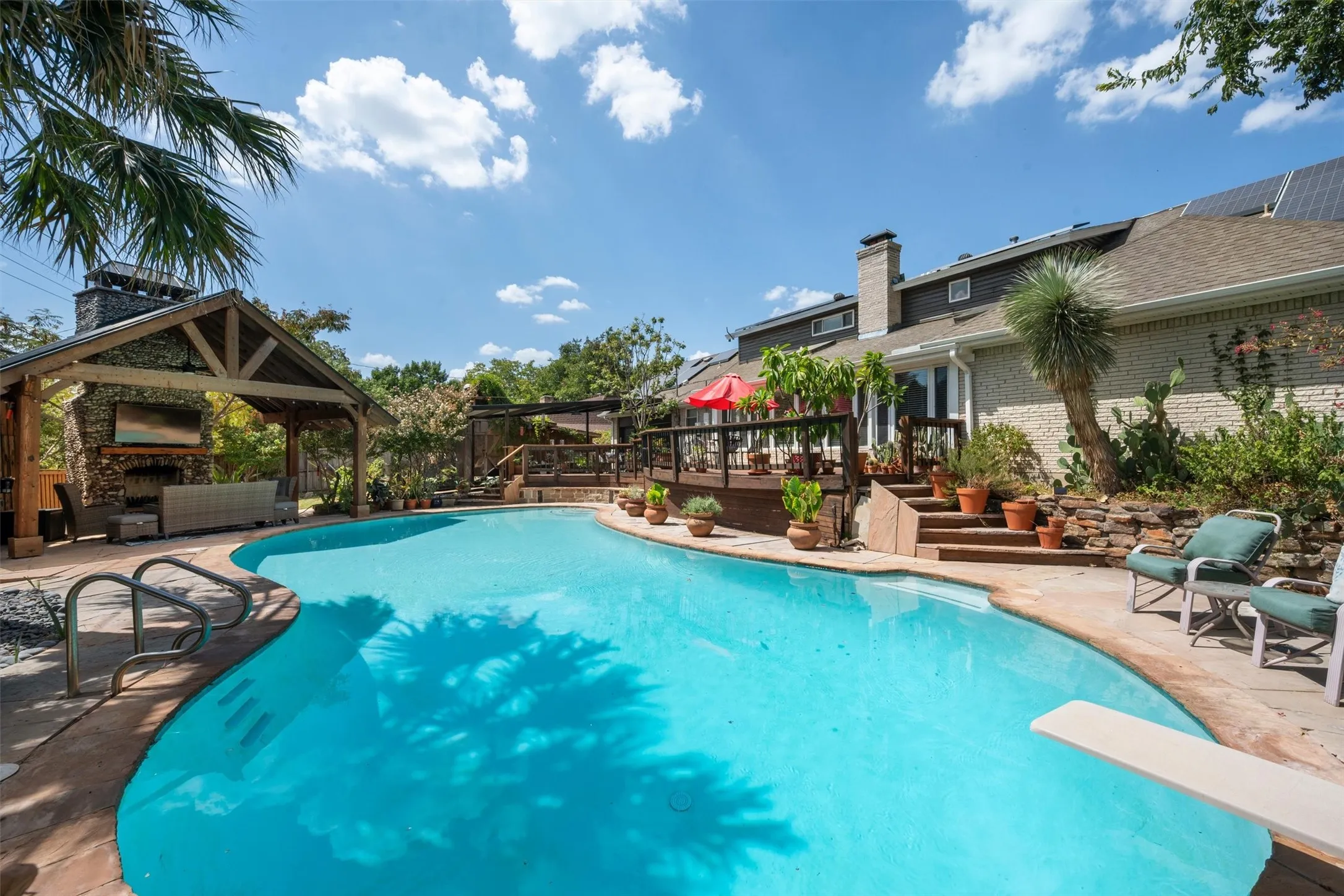 Expansive backyard featuring a custom pool, covered outdoor living area with stone fireplace, multi-level wood deck, and solar panels