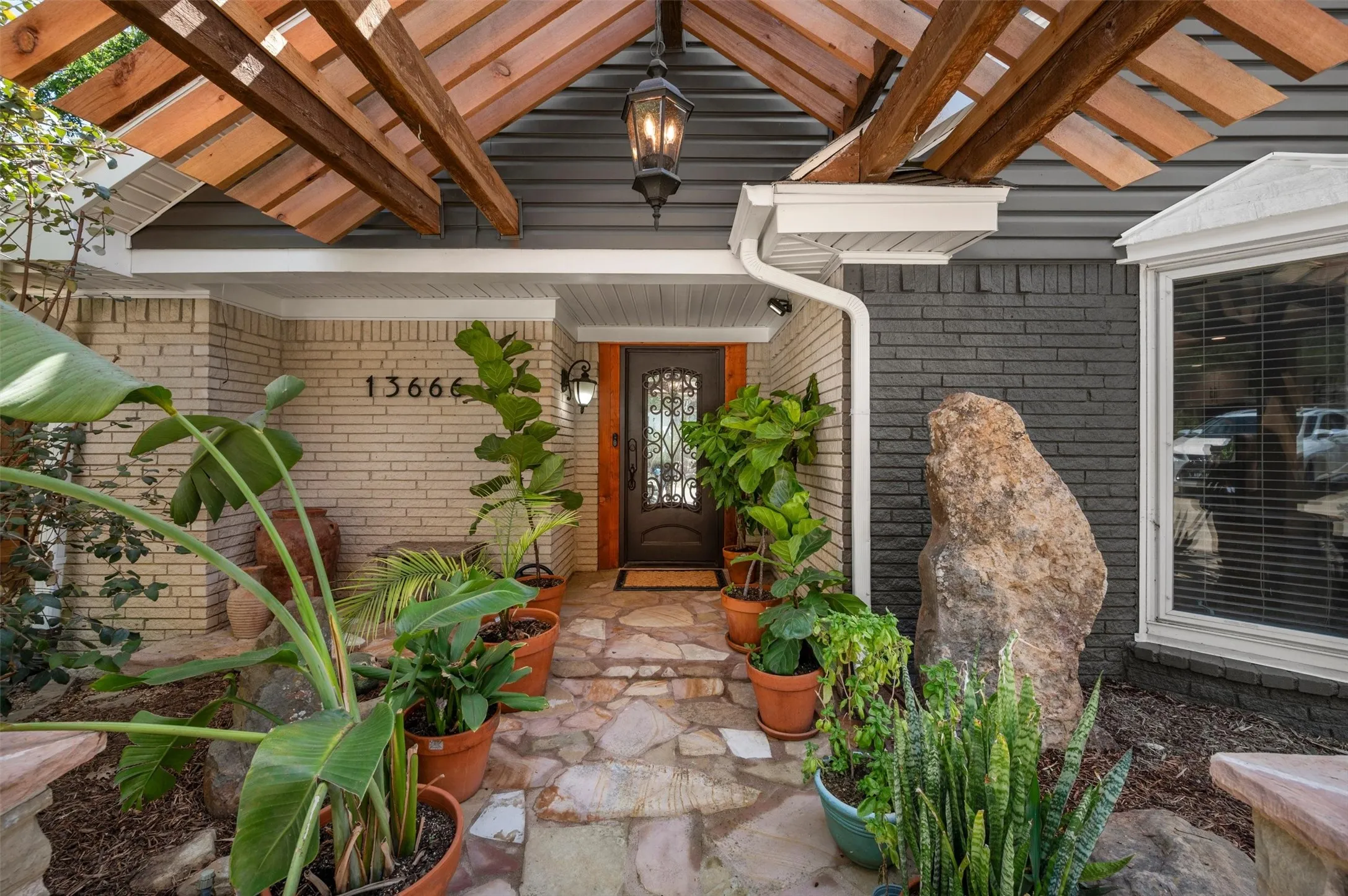 Stone pathway leading to an ornate entry door with decorative glass, complemented by a covered entry with exposed wooden beams