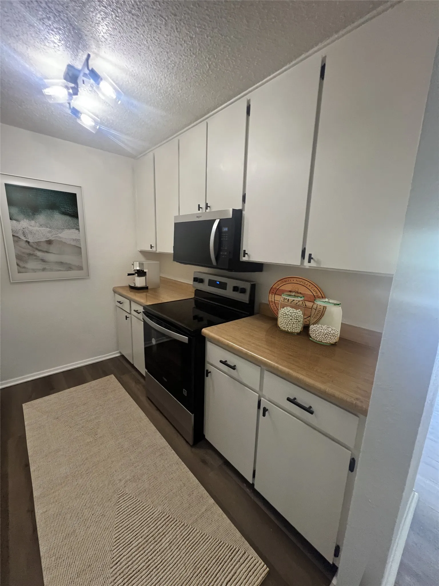 Kitchen featuring stainless steel electric range oven, dark wood-type flooring, white cabinets, a textured ceiling, and light countertops