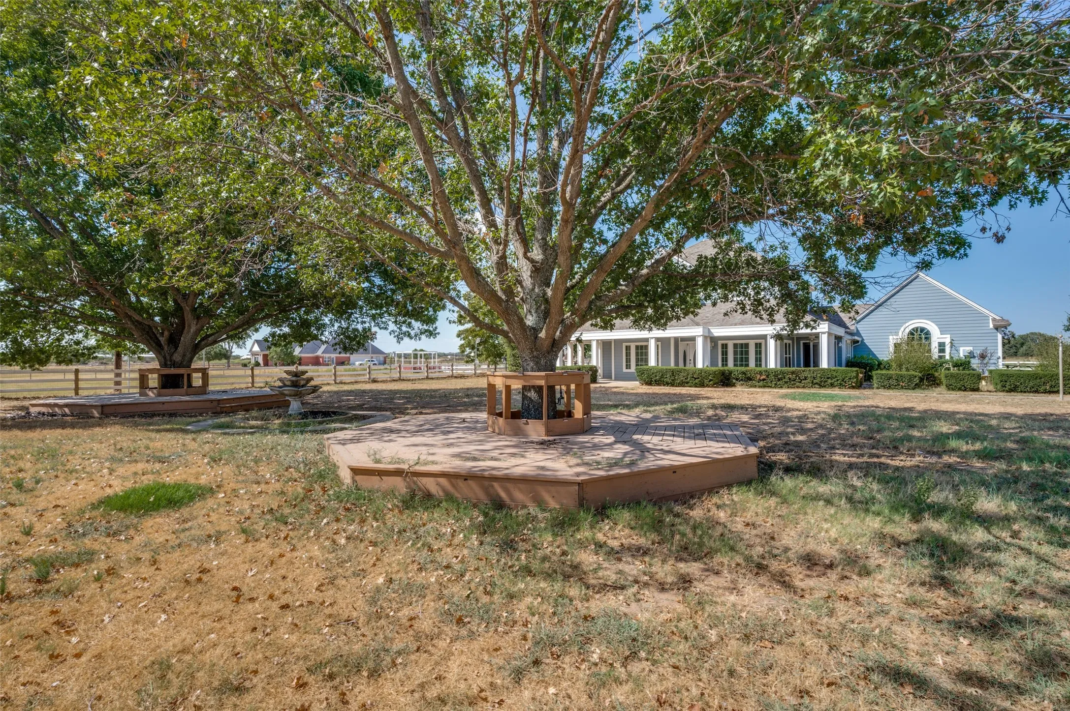 Expansive yard featuring mature trees, a multi-tiered fountain, and a light blue exterior with white trim