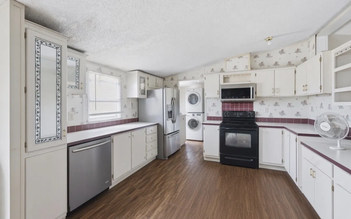 Kitchen with wood-finish flooring, white cabinetry, a stainless steel dishwasher, a black range with an overhead microwave, and a visible window