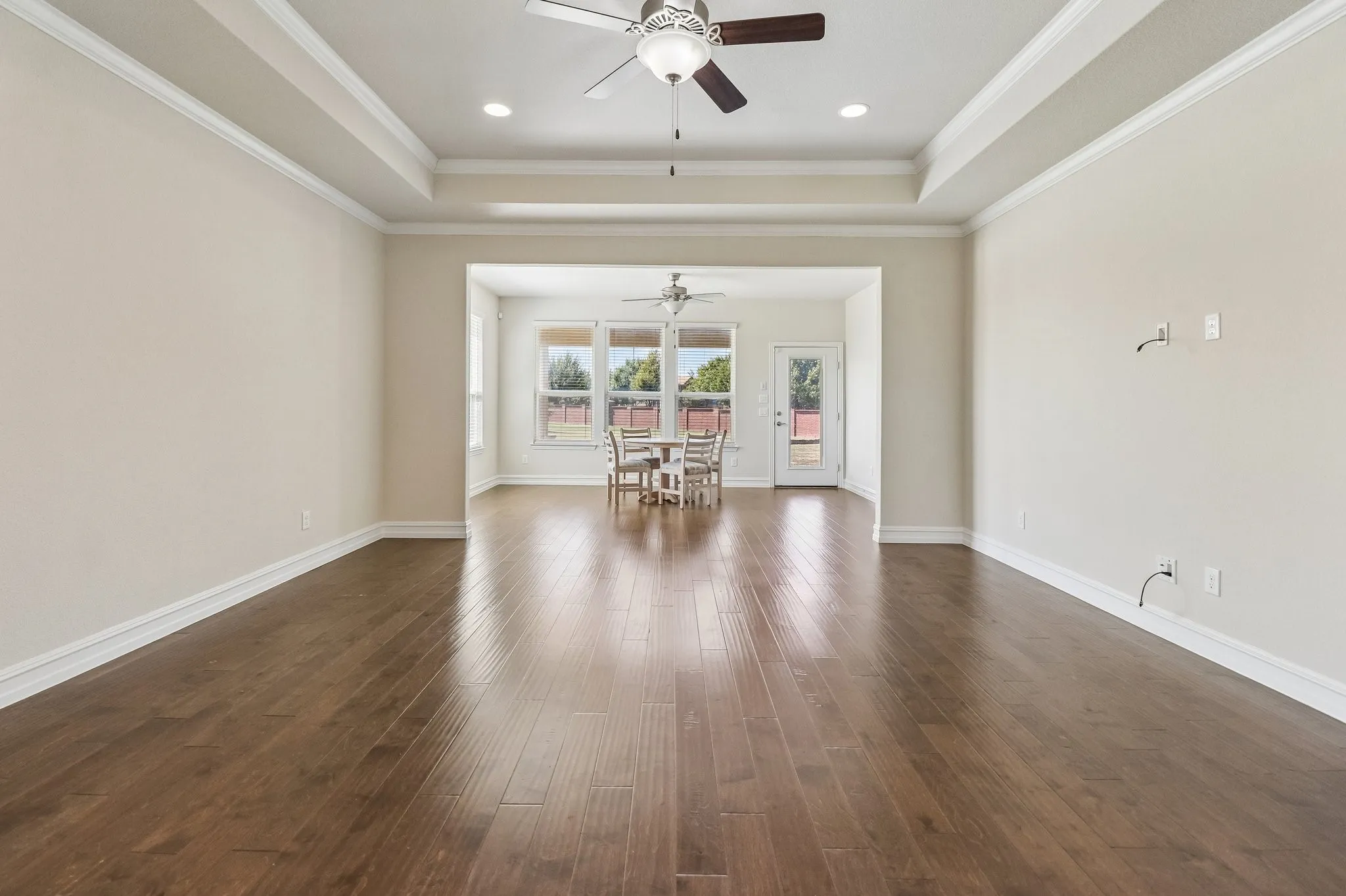 Spacious interior featuring wood-finish flooring, a tray ceiling with recessed lighting, and a ceiling fan
