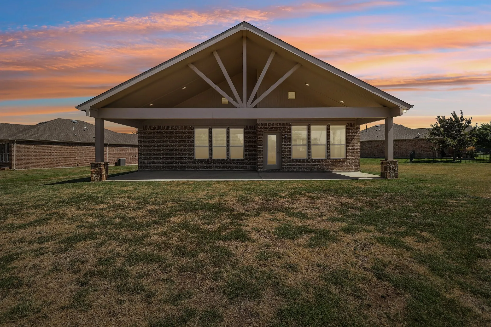 Expansive backyard featuring a covered patio with exposed beams, brick exterior, and a glass-paneled door