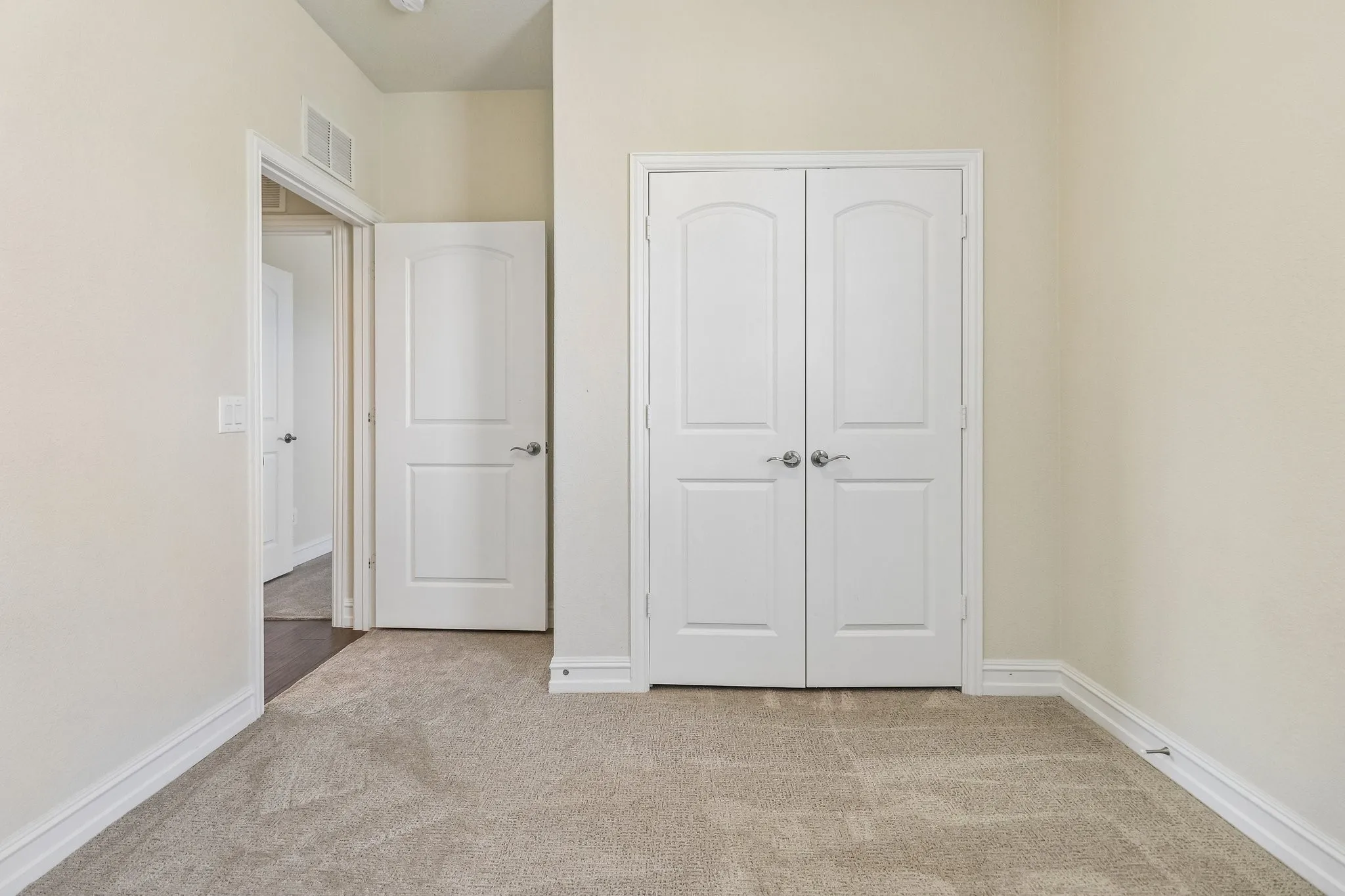 Carpeted flooring with white trim, featuring a bi-fold door closet and an arched doorway