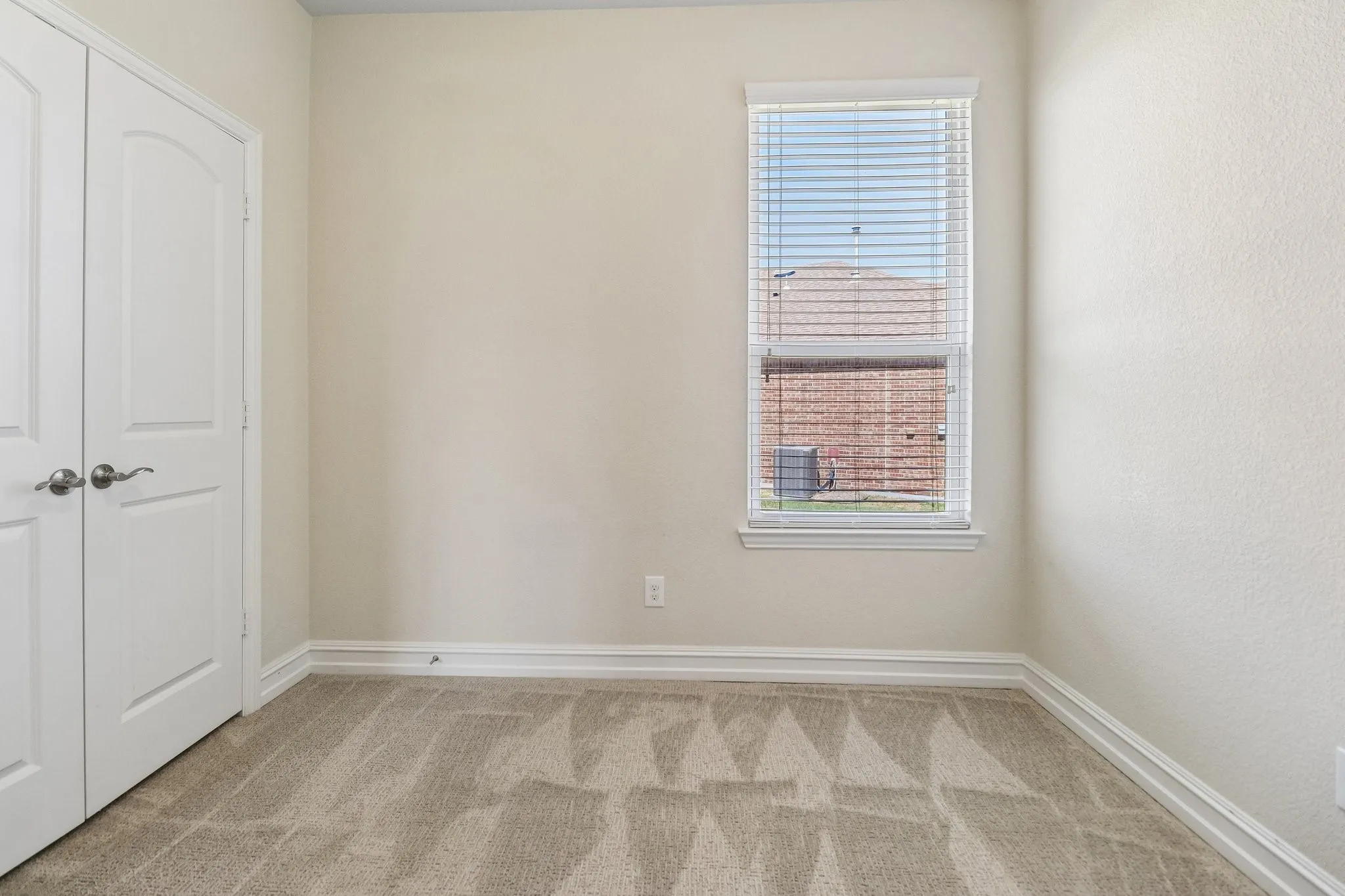 Neutral wall finishes with white trim, a single window with blinds, and light-toned carpet flooring