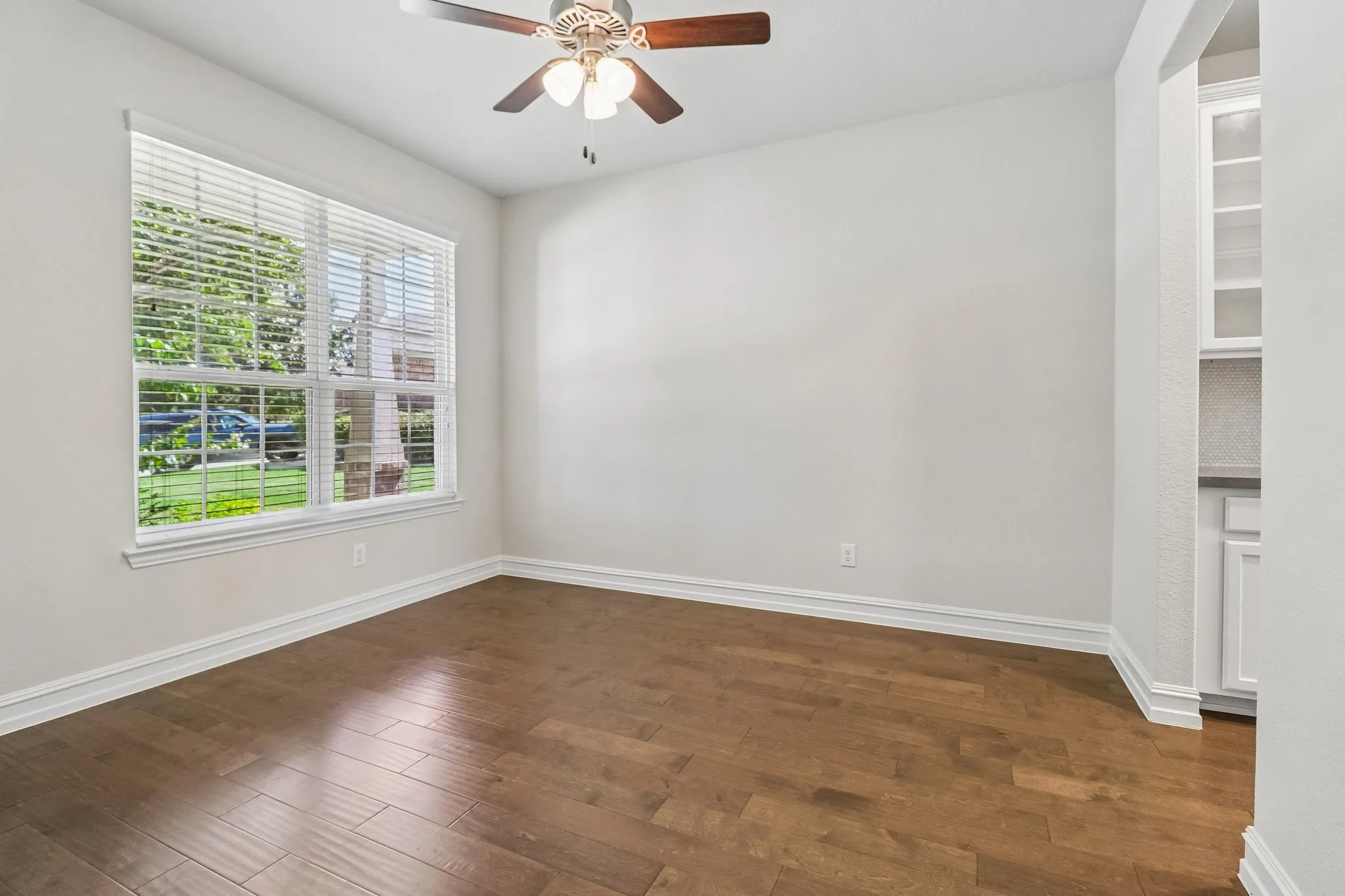 Wood-finish flooring, ceiling fan with light fixture, large window with blinds, and built-in cabinetry