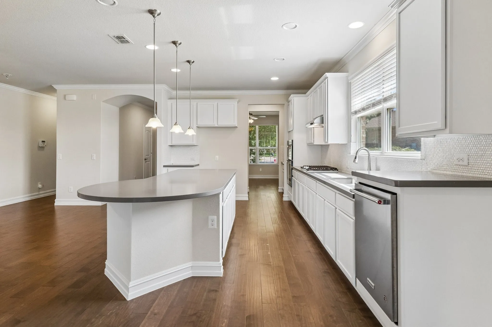 Kitchen featuring wood-finish flooring, white cabinetry, a large island with a dark countertop, stainless steel appliances, and a tiled backsplash