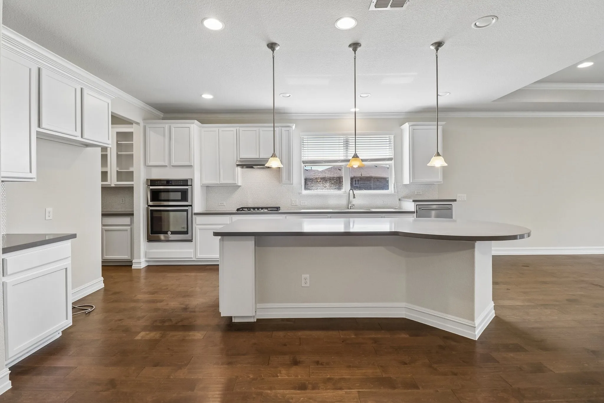 Kitchen featuring wood-finish flooring, white cabinetry, dark countertops, a built-in double oven, and a kitchen island with pendant lighting