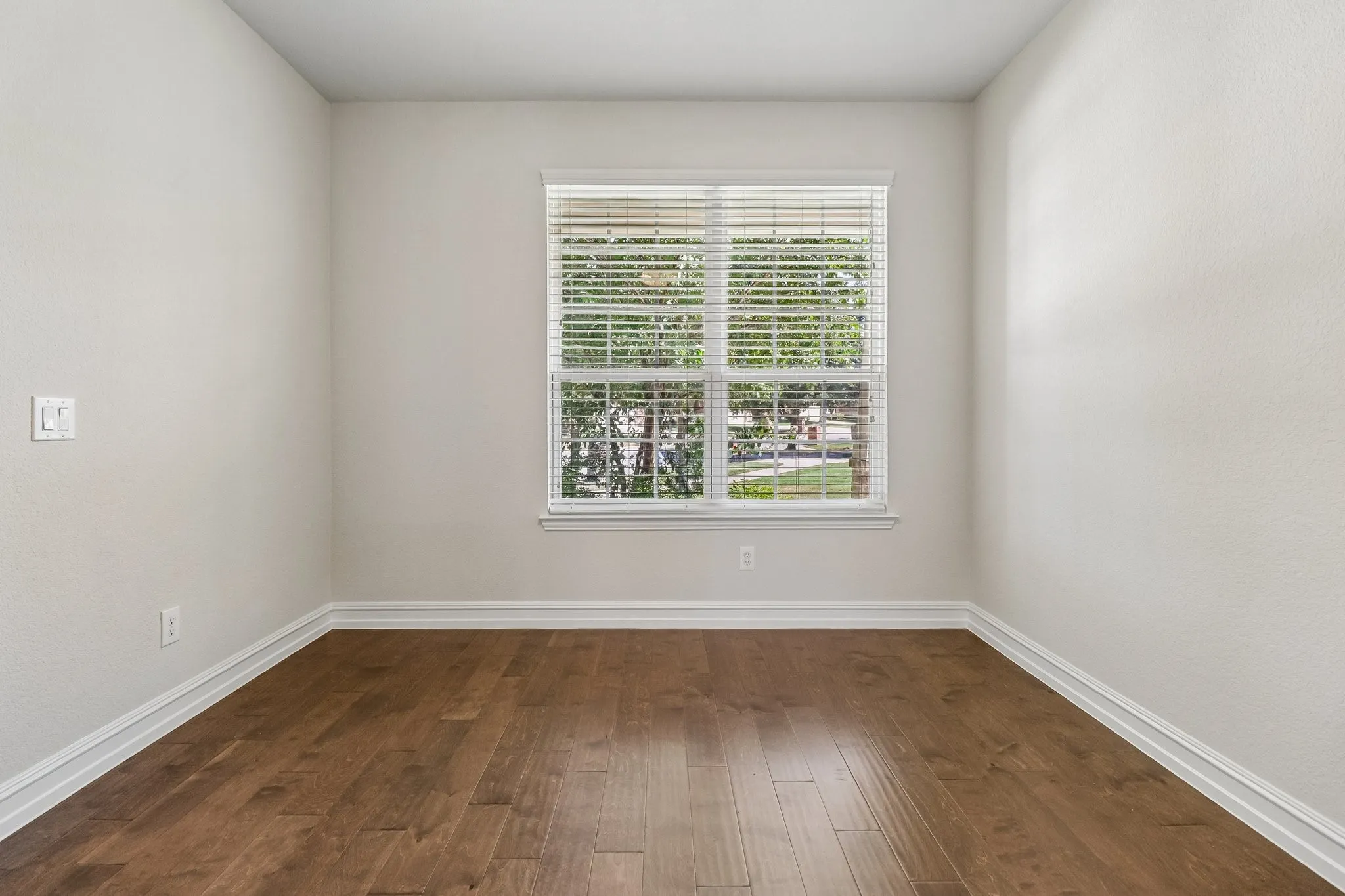 Room with wood-finish flooring, white baseboards, and a window with blinds