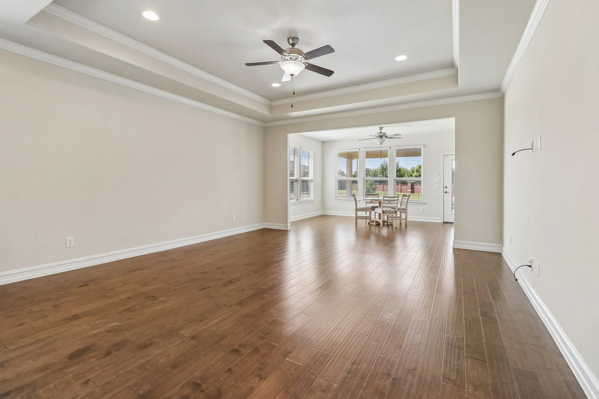Spacious room featuring wood-finish flooring, a tray ceiling, recessed lighting, and a ceiling fan